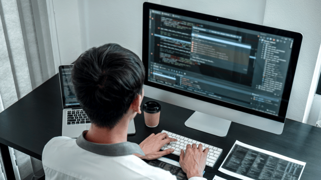 Software developer coding on a desktop computer with multiple screens displaying code.