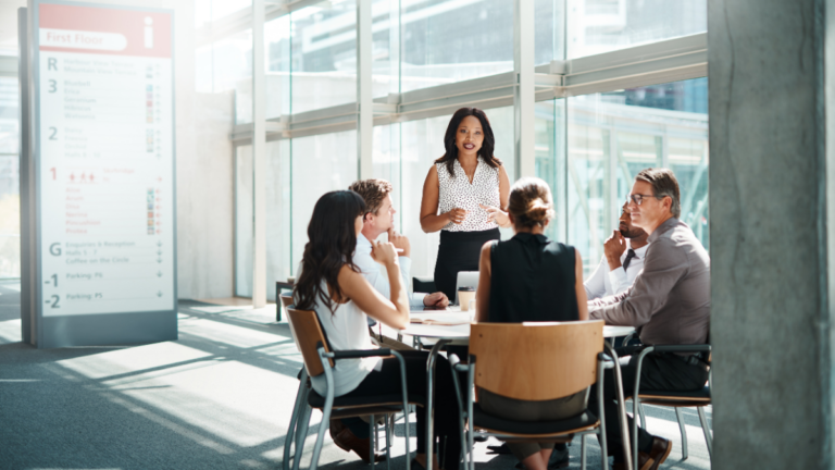 Businesswoman presenting to a group of colleagues during a meeting in a modern office setting.