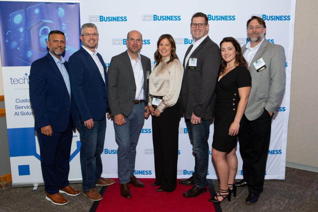 Group photo of the Altitude Marketing team standing on a red carpet in front of a Lehigh Valley Business banner at the Fastest Growing Companies event. Team members are dressed in business attire, smiling, and wearing event badges.