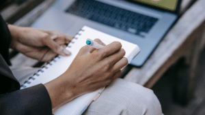 person writing on notebook with laptop in front of them working on content syndication