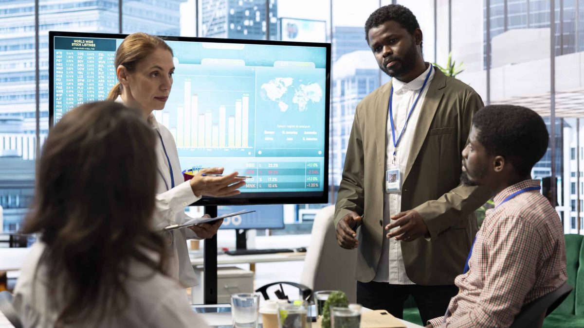 Financial expert briefing his team members about new enterprise objectives, showing analysis of their budget and expenses on interactive board. Resource allocation and project planning meeting.